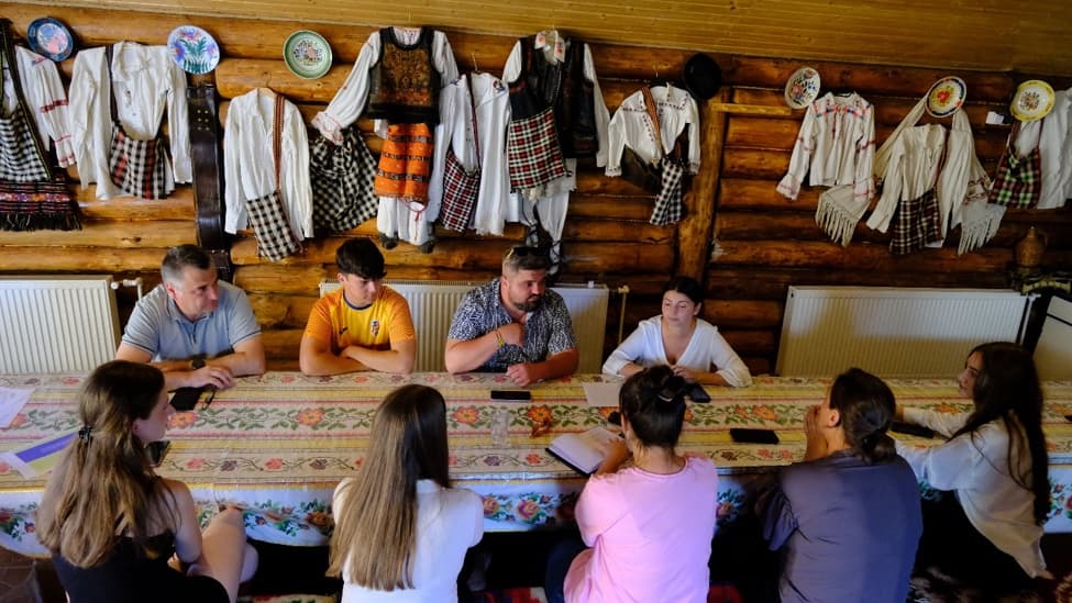 Grupul de inițiativă în jurul mesei, sub costumele populare de pe perete